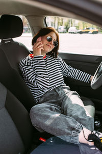 Portrait of a young brunette woman driving in a car using a smartphone