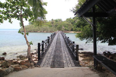 Pier over sea by trees against sky