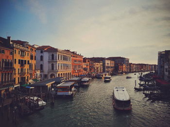 Boats moored in canal by buildings in city against sky