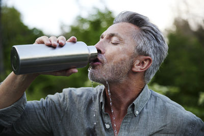 Thirsty man spilling while drinking water from bottle in forest