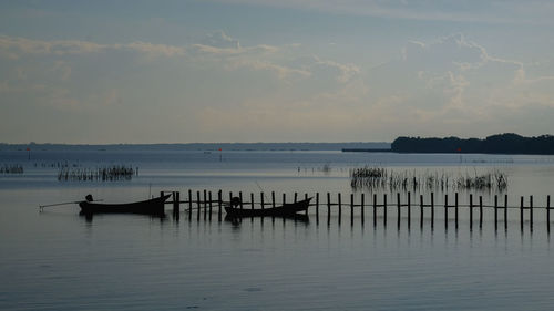 Silhouette wooden posts in sea against sky