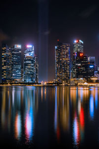 Illuminated city by river against sky at night