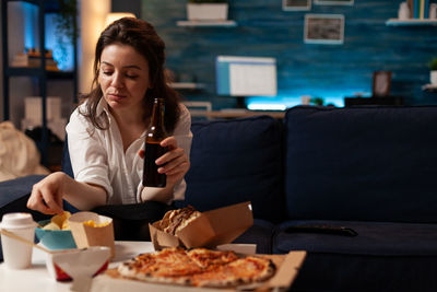 Woman eating food while sitting on sofa at home