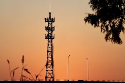 Low angle view of silhouette communications tower against sky during sunset