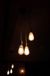 Low angle view of illuminated light bulb hanging against black background