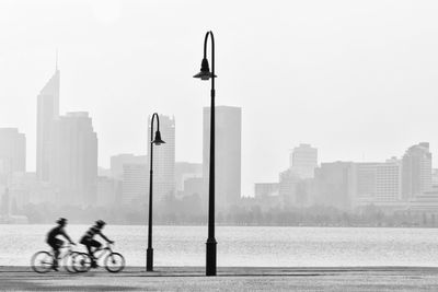 People riding bicycle on street against buildings in city