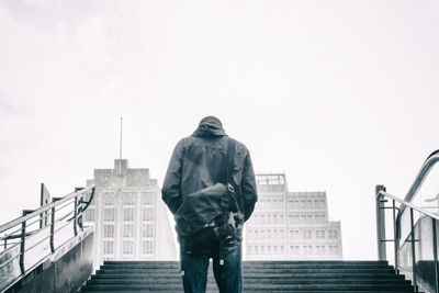 Rear view of man at staircase against sky during rainy season