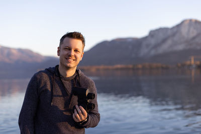 Portrait of man holding binocular against lake