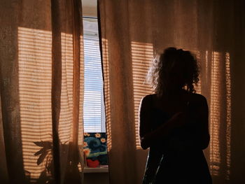 Rear view of woman standing by window at home