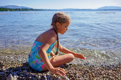 Girl has fun and plays with stones on pebble beach at geneva lake, summer vacations and travel