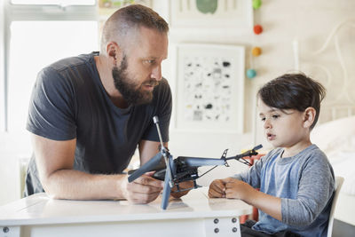 Father holding toy vehicle while looking at son in bedroom