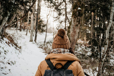 Rear view of woman in winter clothes hiking in nature. forest, snow, exploring, backpack.