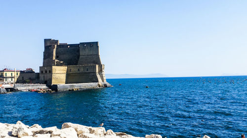 Building by sea against clear blue sky