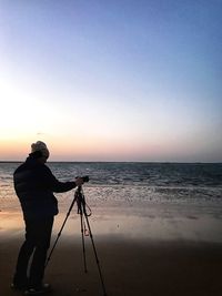 Man photographing at beach against sky during sunset