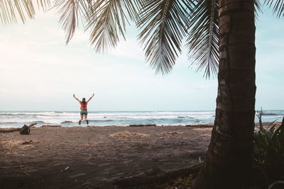 Rear view of woman with arms raised jumping at beach