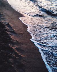 High angle view of surf on shore at beach during sunset