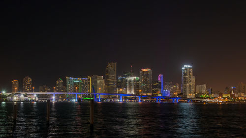 Illuminated buildings by river against sky at night