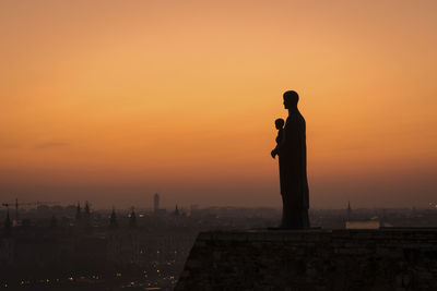 Silhouette man standing by building against sky during sunset