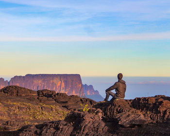 Rear view of man standing on rock against sky
