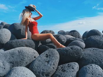 Woman sitting on rock in sea against sky