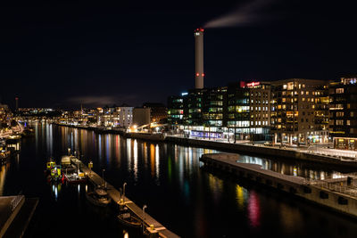 Illuminated buildings by river against sky at night