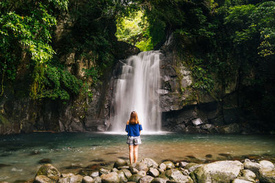 Rear view of woman looking at waterfall while standing on rocks