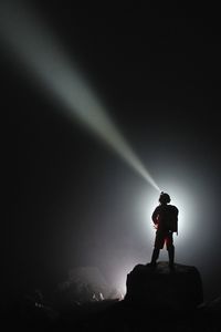 Man using flashlight while standing on rock at night