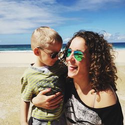 Close-up of happy mother and son on beach against sky