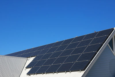 Low angle view of solar panels on roof against clear blue sky
