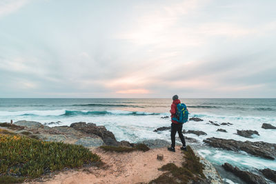 Rear view of woman standing at beach against sky during sunset