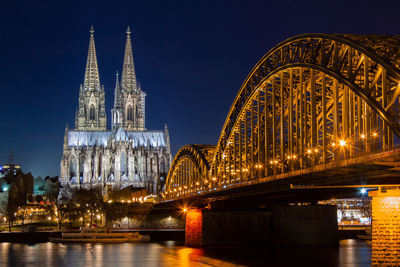 Illuminated bridge over river in city at night