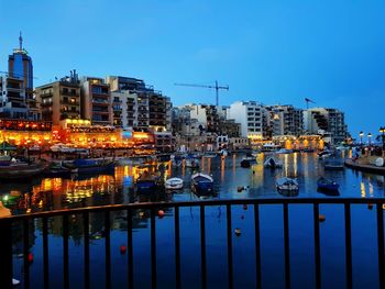 Illuminated buildings by river against sky at dusk