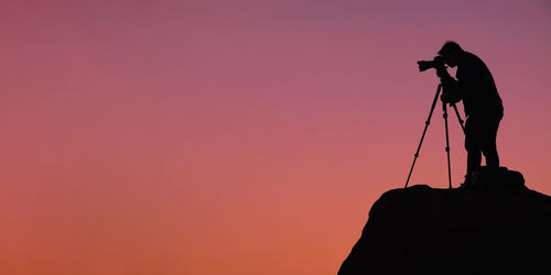 Silhouette man standing on rock against sky during sunset
