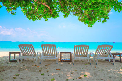 Empty chairs on beach against sky