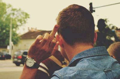 Rear view of man showing middle finger against clear sky