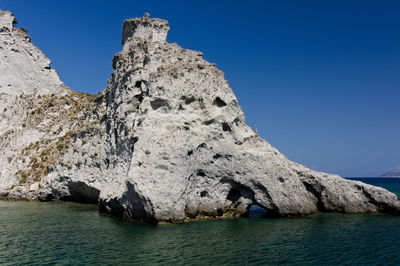 Rock formations in sea against clear blue sky