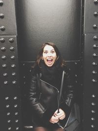 Portrait of surprised woman standing by black wall