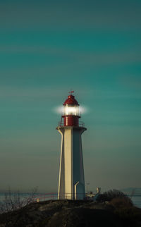 Lighthouse by sea against sky during sunset