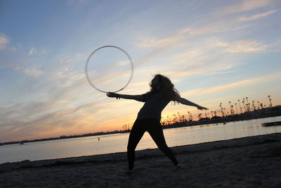 Full length of woman dancing with plastic hoop at beach during sunset