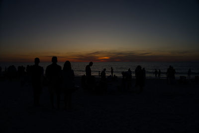 Silhouette people on beach against sky during sunset