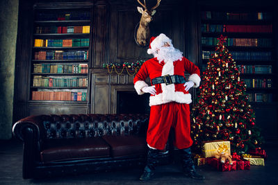 Man wearing santa claus costume standing by christmas tree at home