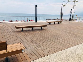 Empty benches on pier by sea against sky