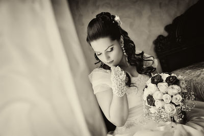 Bride holding bouquet while sitting on bed at home