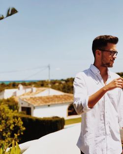 Young man looking away while standing against sky