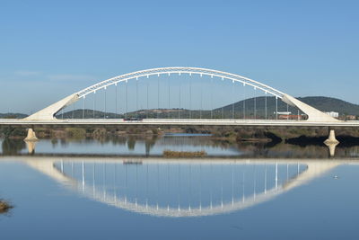 Bridge over river against clear sky and its reflection