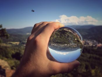 Cropped hand of person holding crystal ball on mountain against sky