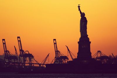 Silhouette statue against factory during sunset