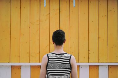 Rear view of man standing against yellow wooden wall