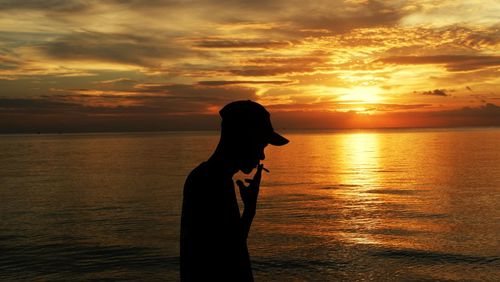 Silhouette man smoking against sea during sunset