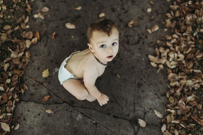 Baby toddler boy in diaper sitting with fall leaves at halloween